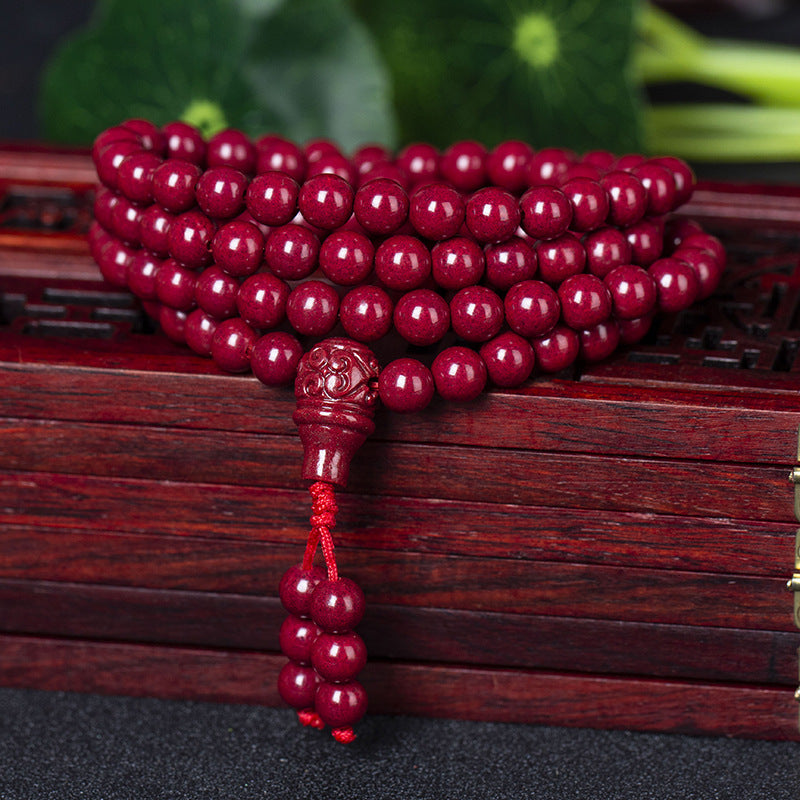 A 108 - bead cinnabar bracelet elegantly placed on a wooden box. The deep - red cinnabar beads shine brightly, and the elaborately carved pendant hints at traditional charm