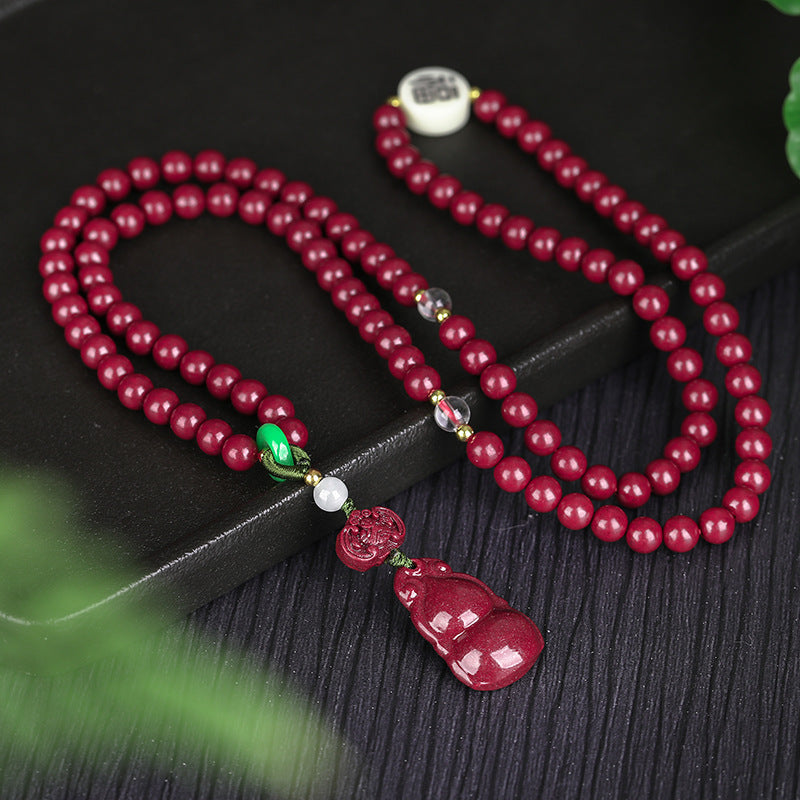 A 108 - bead cinnabar jewelry item placed on a black tray Showcasing deep - red cinnabar beads, colorful gemstone accents, and a striking cinnabar gourd pendant.