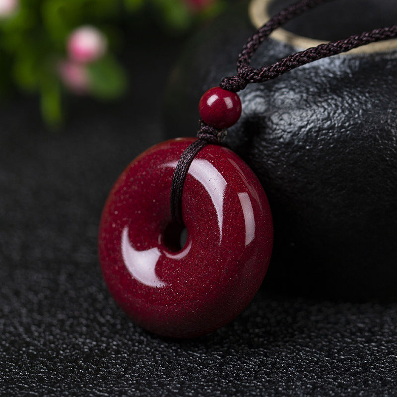 A cinnabar donut pendant with a small cinnabar bead on the cord, hanging beside a black pot. The pendant's deep - red color shines brightly.