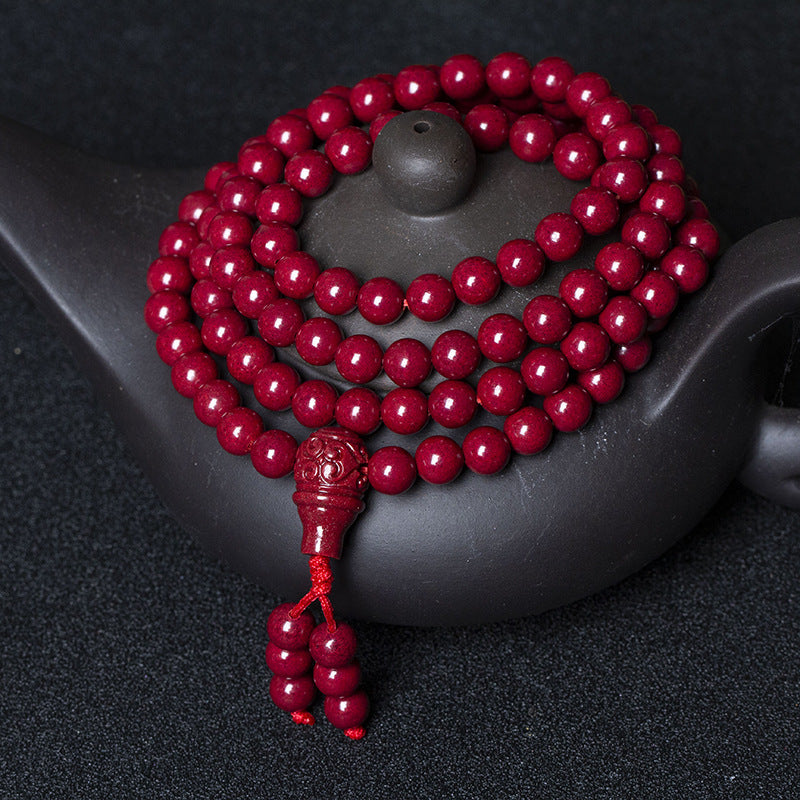 The 108 - bead cinnabar bracelet coiled on a black teapot showcases uniform red beads and a detailed carved pendant, exuding an air of antiquity.