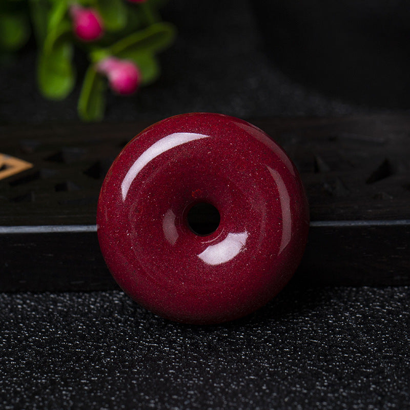 A cinnabar donut pendant placed on a dark - colored wooden object, showing its smooth and shiny surface.