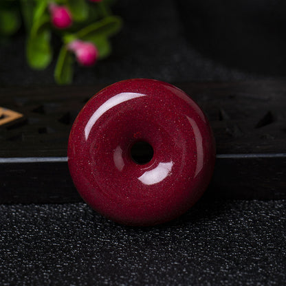 A cinnabar donut pendant placed on a dark - colored wooden object, showing its smooth and shiny surface.