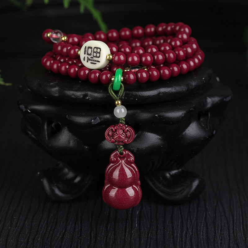 The 108 - bead cinnabar jewelry coiled on a black container Highlighting the white "108" bead, green and white gemstone details, and the exquisitely carved cinnabar gourd.