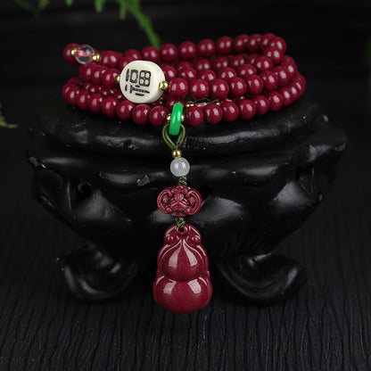 The 108 - bead cinnabar jewelry coiled on a black container Highlighting the white "108" bead, green and white gemstone details, and the exquisitely carved cinnabar gourd.