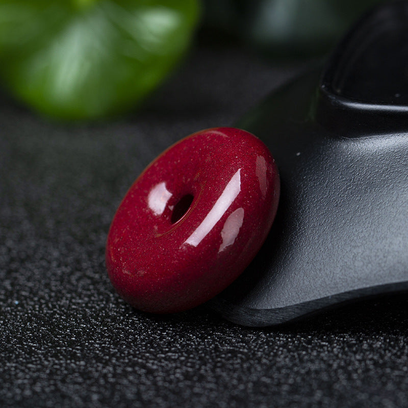 A cinnabar donut pendant leaning against a black plate, highlighting its round shape and rich red color.