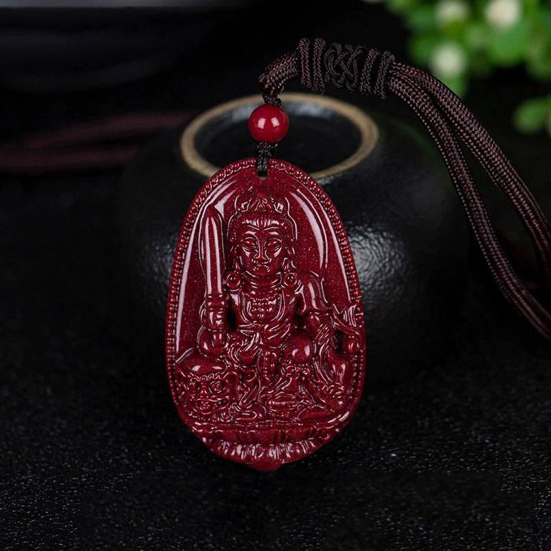 A cinnabar pendant featuring a deity holding a sword - like object, laid out beside a black pot. The red bead on the cord stands out.